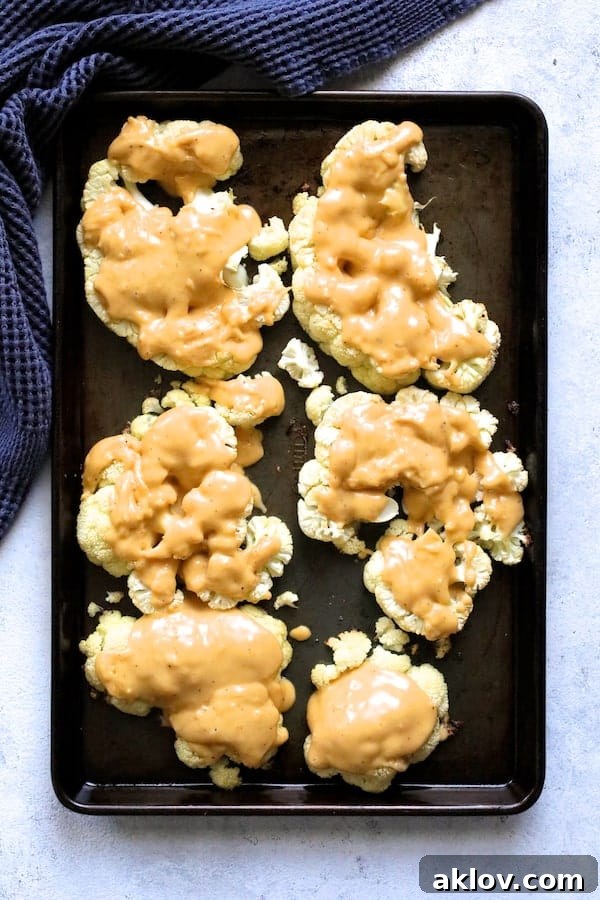Roasted cauliflower steaks completely covered in a rich cheese sauce on a baking sheet.