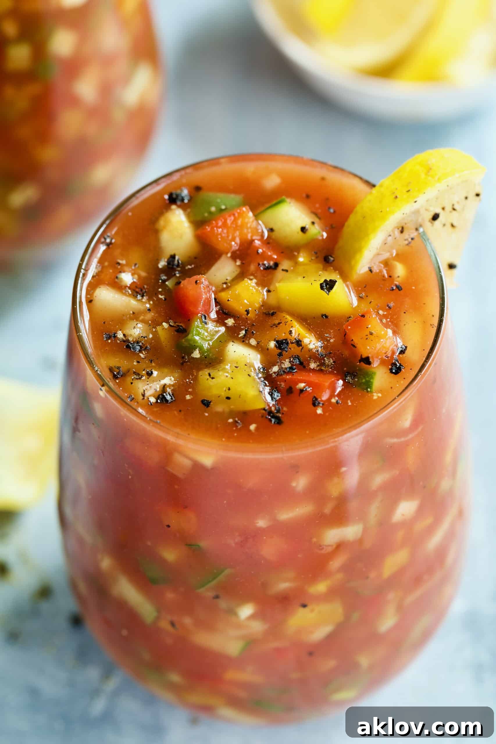 A single glass of the Best Vegetable Gazpacho, perfectly garnished with a lemon wedge, against a soothing light blue backdrop.