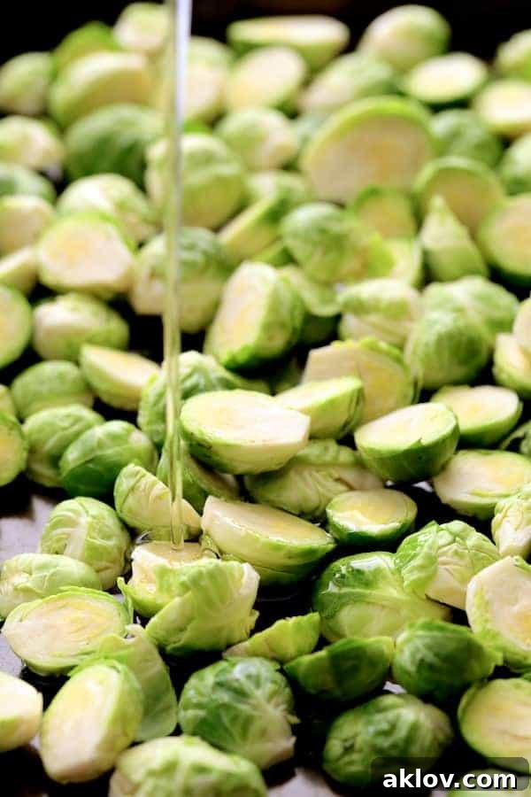 Fresh Brussels sprouts being generously drizzled with oil on a baking sheet before roasting, ensuring a perfect crisp.