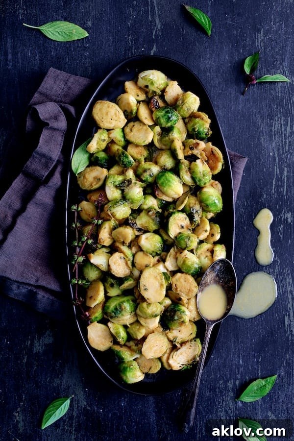 Beautifully plated Roasted Brussels Sprouts with Thai Green Curry Butter on a sleek black platter, with drops of the rich butter visible, highlighting the dish's allure.
