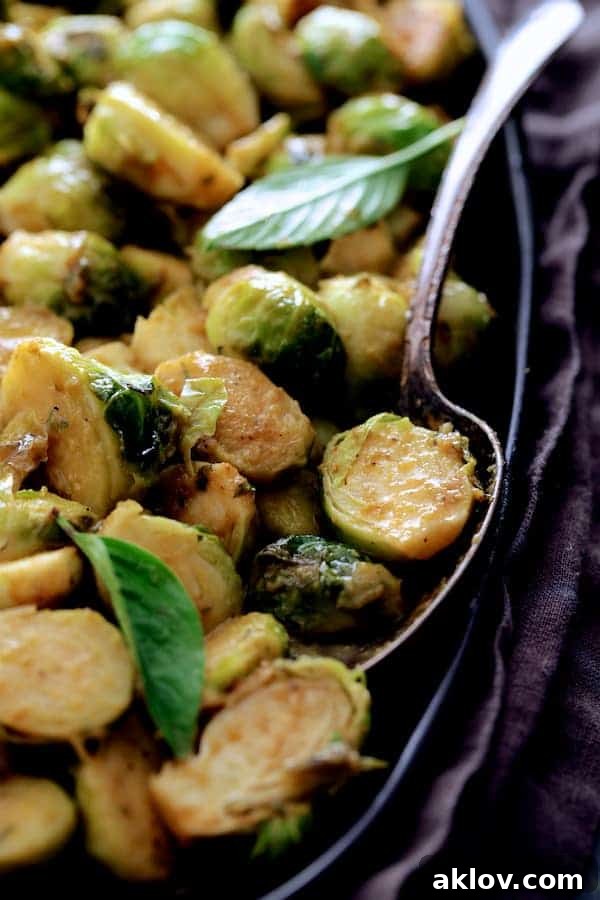 An inviting close-up of Roasted Brussels Sprouts with Thai Green Curry Butter on a black platter, elegantly garnished with fresh Thai basil leaves, enhancing its visual appeal and aromatic profile.