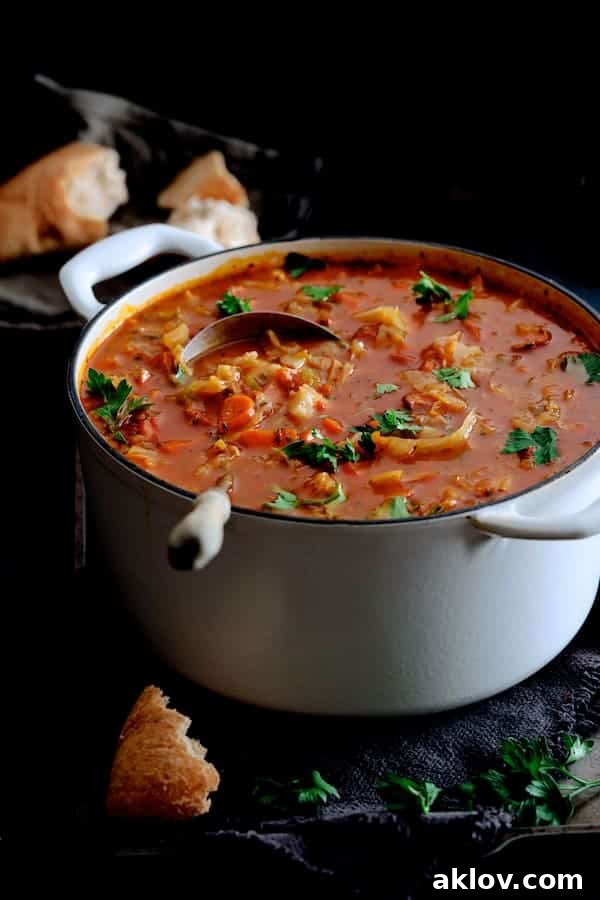 A large serving of Old-Fashioned Potato Cabbage and Kielbasa Soup in a white enameled Dutch oven, surrounded by crusty bread, perfect for dipping.