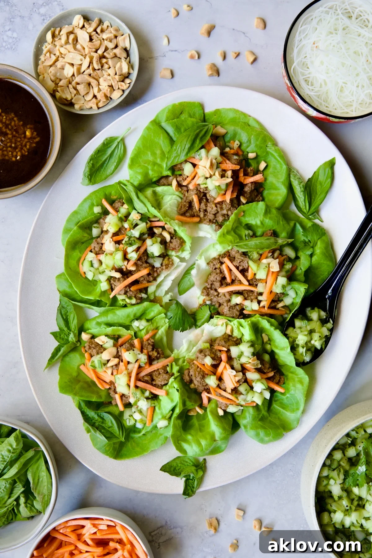 Vietnamese Beef Lettuce Wraps on oval white platter with lime wedges and accompaniments around it.
