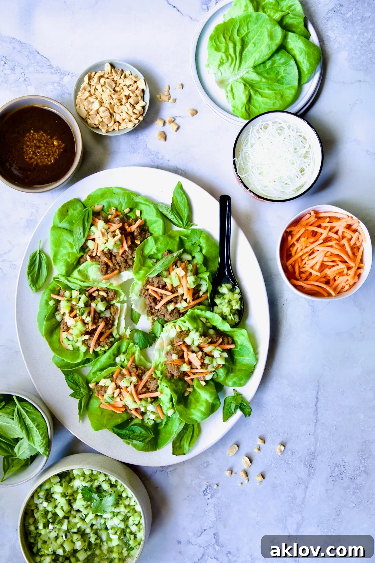 Vietnamese Beef Lettuce Wraps on oval white platter with lime wedges and accompaniments around it.
