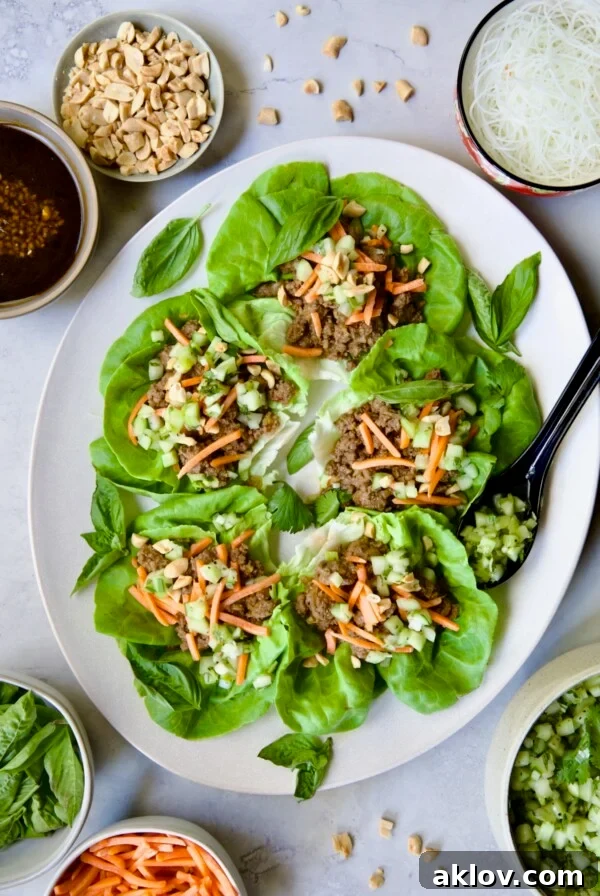 Vietnamese Beef Lettuce Wraps on oval white platter with lime wedges and accompaniments around it.