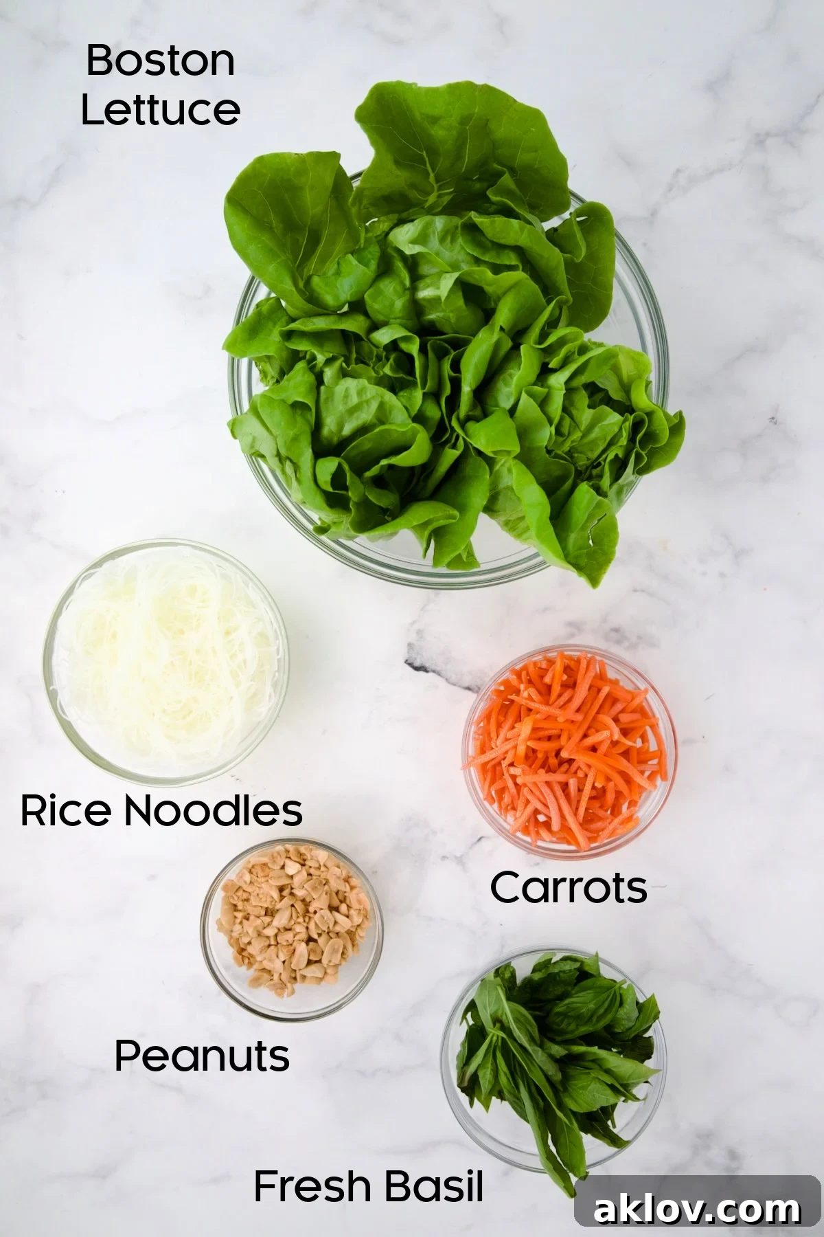 Lettuce, rice noodles, carrots, peanuts and fresh basil in glass bowls.