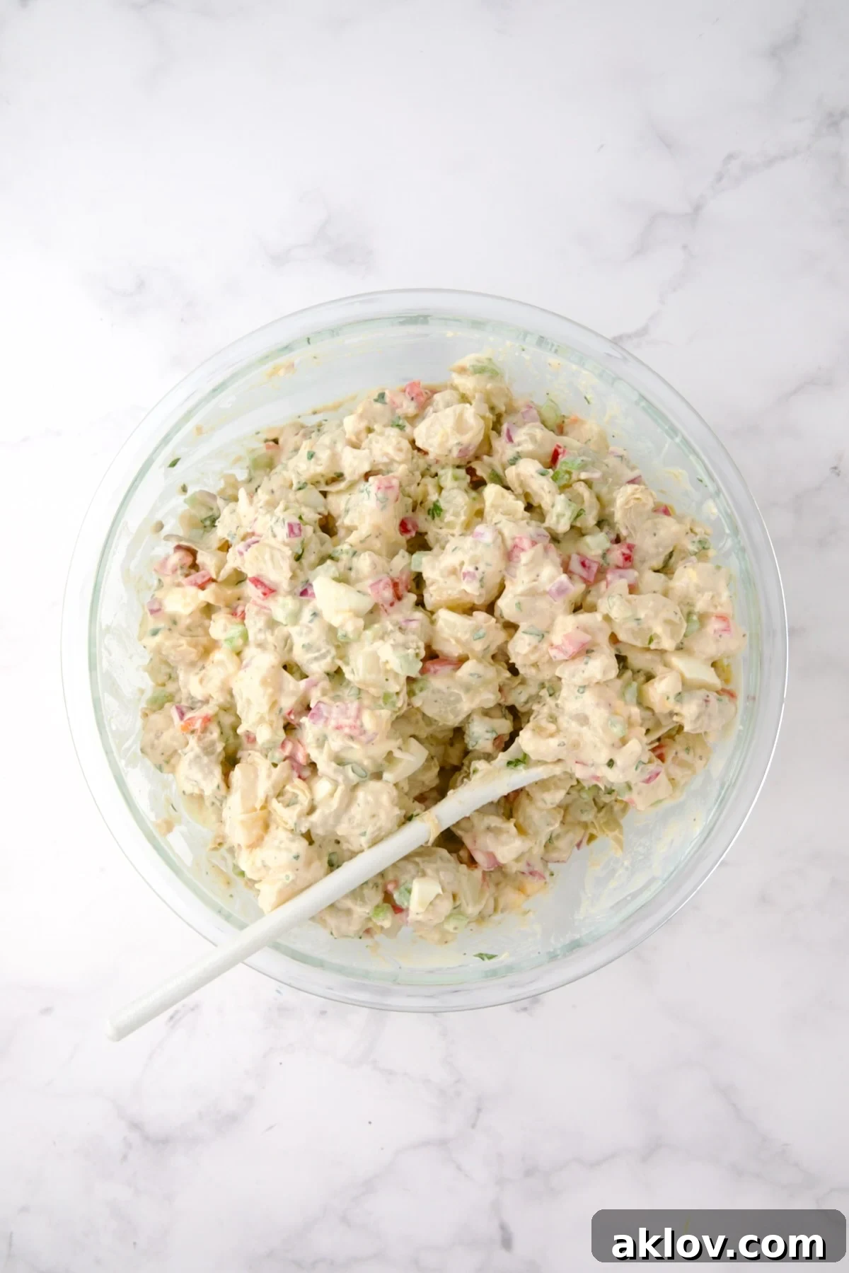 The finished Horseradish Potato Salad in a glass bowl, perfectly mixed with dressing and eggs, with a white mixing spoon, showcasing its creamy and well-combined texture.