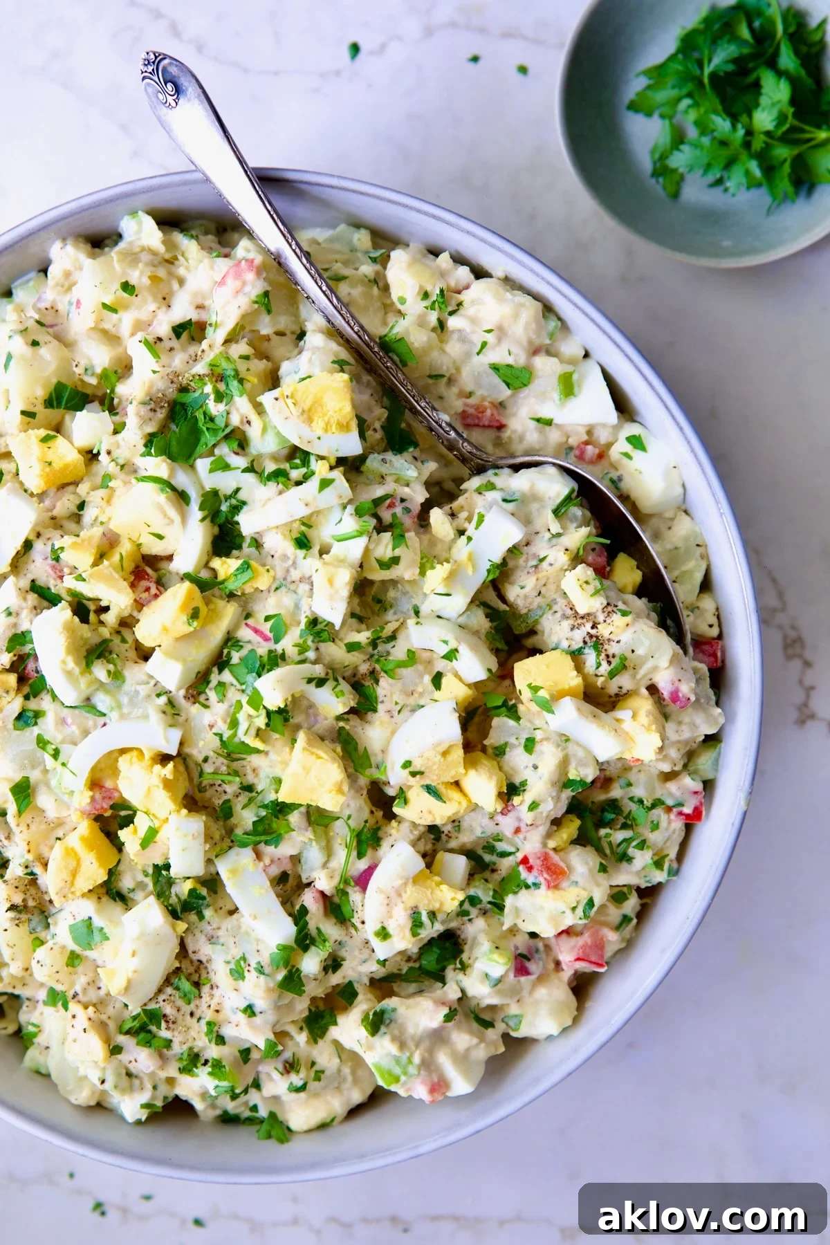 A vibrant and fresh serving of Horseradish Potato Salad in a light blue bowl, generously garnished with green herbs, inviting enjoyment.