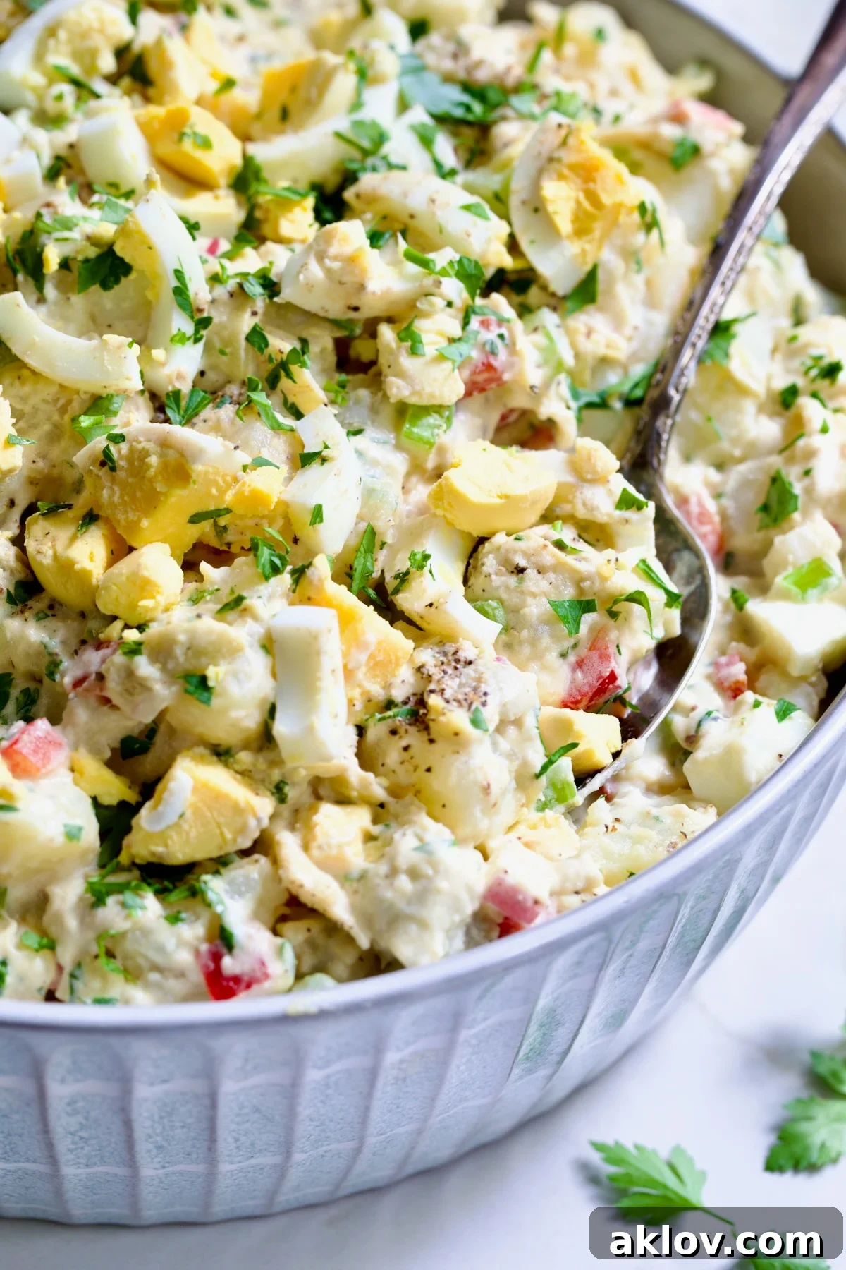 Horseradish Potato Salad with Artichokes served in a beautiful light blue ceramic bowl, garnished with fresh chopped parsley and featuring a silver serving spoon, showcasing its inviting texture.