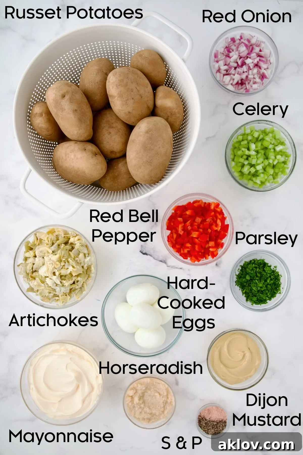 All the fresh ingredients meticulously laid out on a kitchen counter for making Horseradish Potato Salad: includes peeled and cubed potatoes, fresh celery stalks, finely chopped red onion, vibrant red bell pepper, artichoke hearts, and hard-boiled eggs.