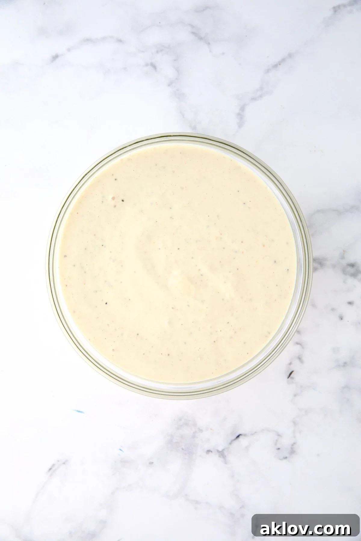 Horseradish potato salad dressing being whisked in a clear glass bowl, showcasing its smooth, creamy texture.