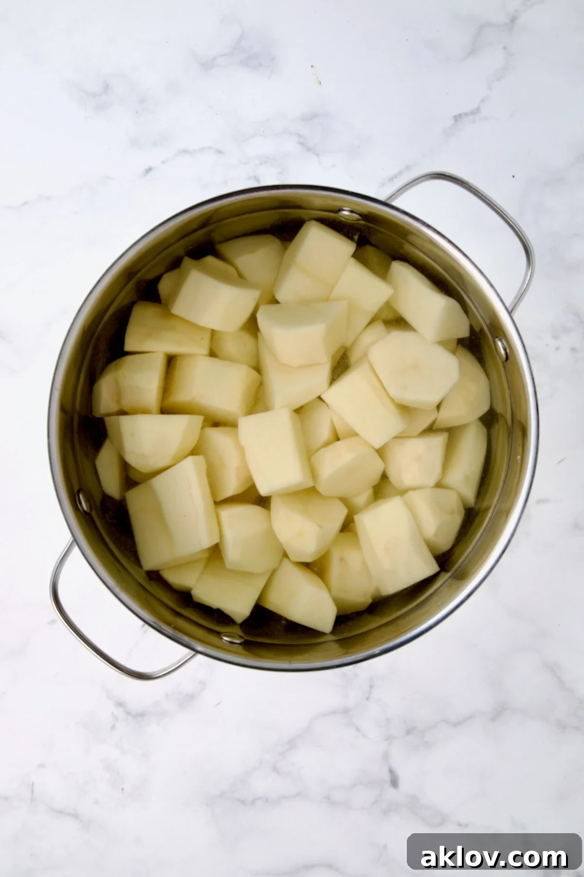 Peeled and uniformly cubed potatoes soaking in cold, generously salted water in a large stainless steel pot, ready for boiling.