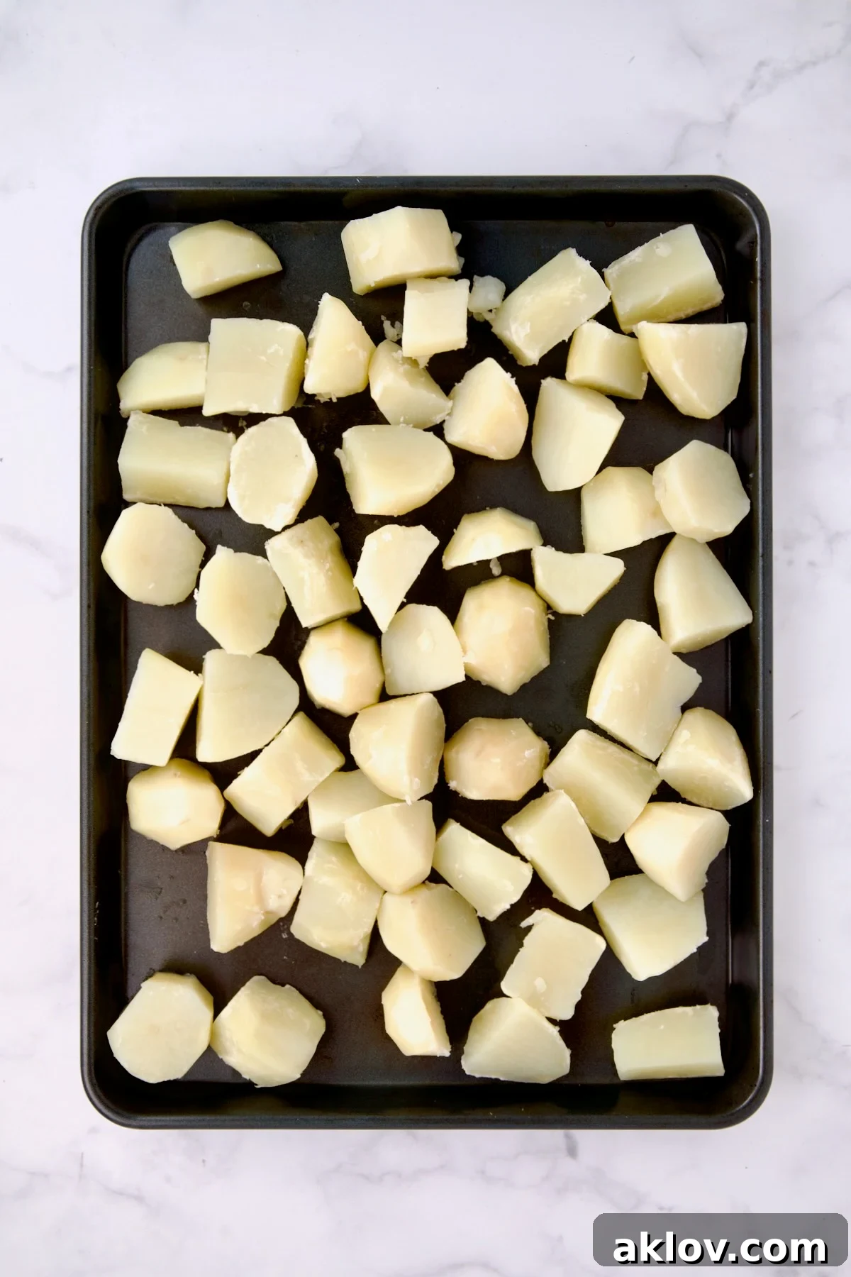 Cooked, uniformly cubed potatoes spread out in a single layer on a chilled rimmed baking sheet to cool quickly and prevent overcooking.