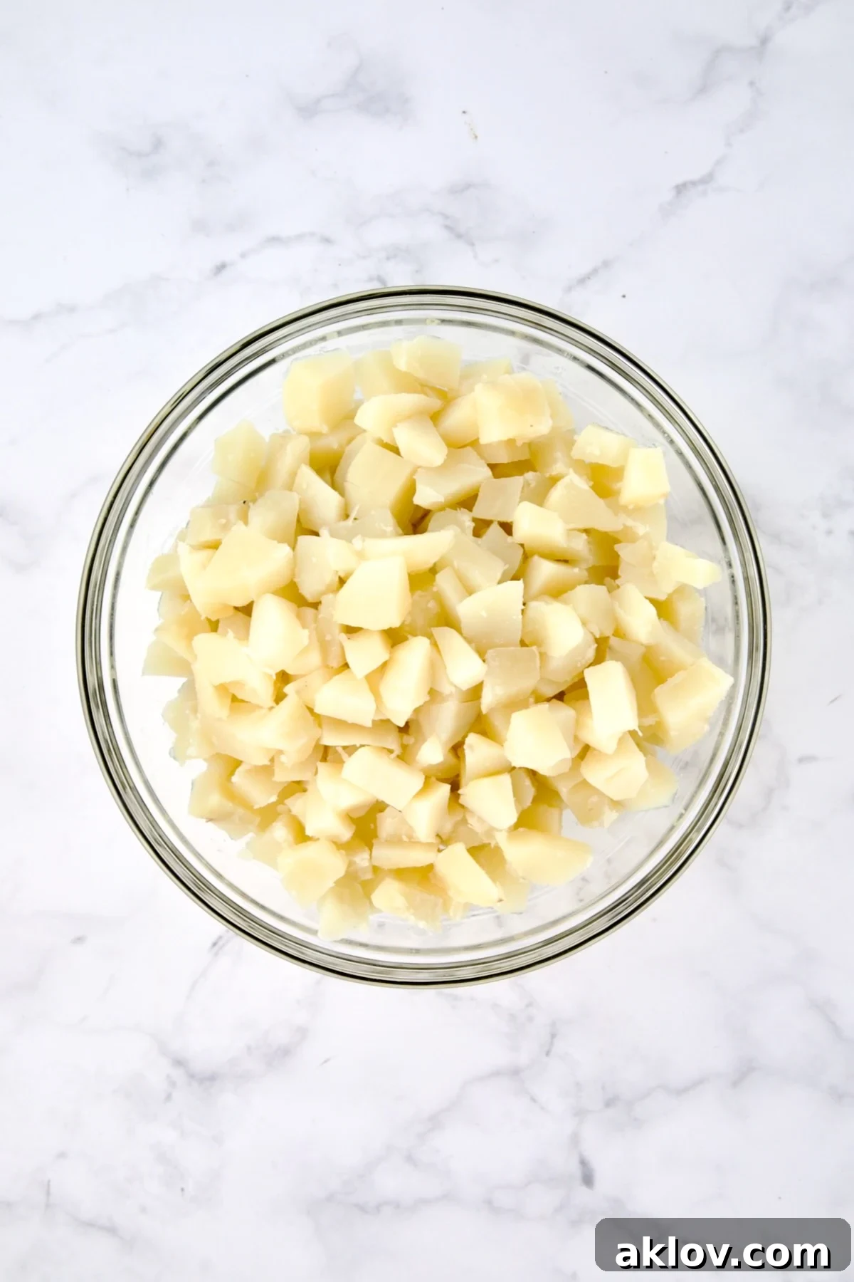 Fully cooled, uniformly bite-sized cubed potatoes placed in a clear glass mixing bowl, ready for combining with other ingredients.