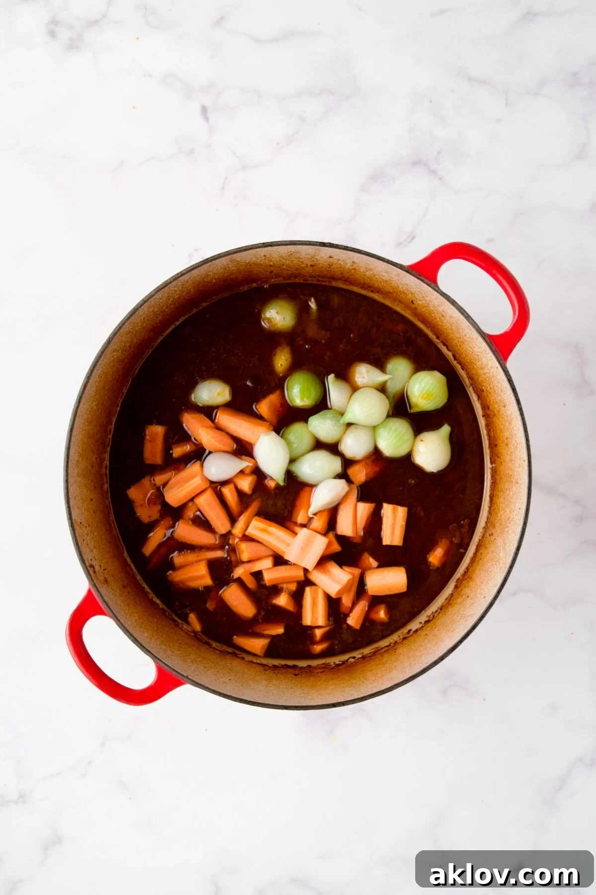 Vibrant carrots and pearl onions added to the rich stew in a red Dutch oven, enhancing its color and flavor.