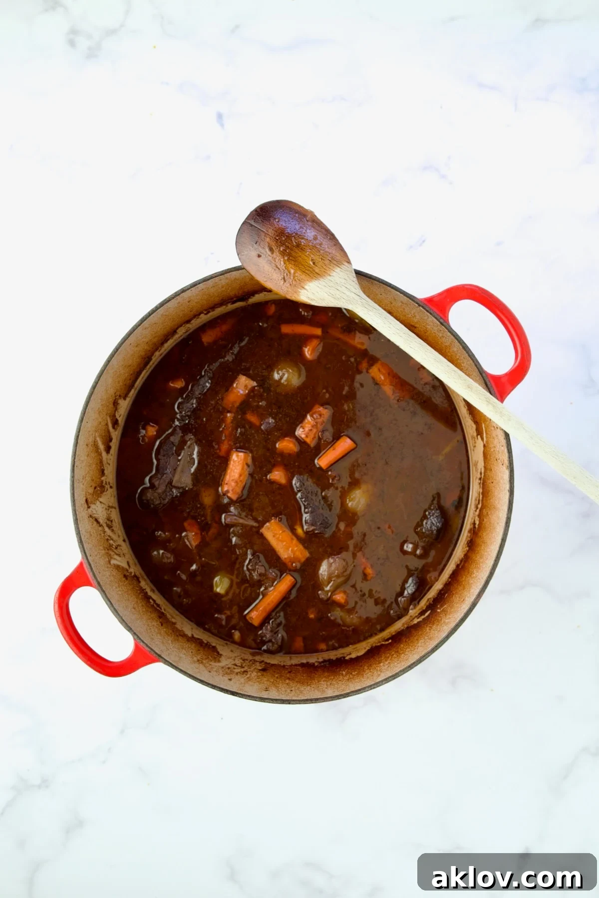 The Boneless Beef Short Ribs Bourguignon simmering in a red Dutch oven with a wooden spoon, before thickening.