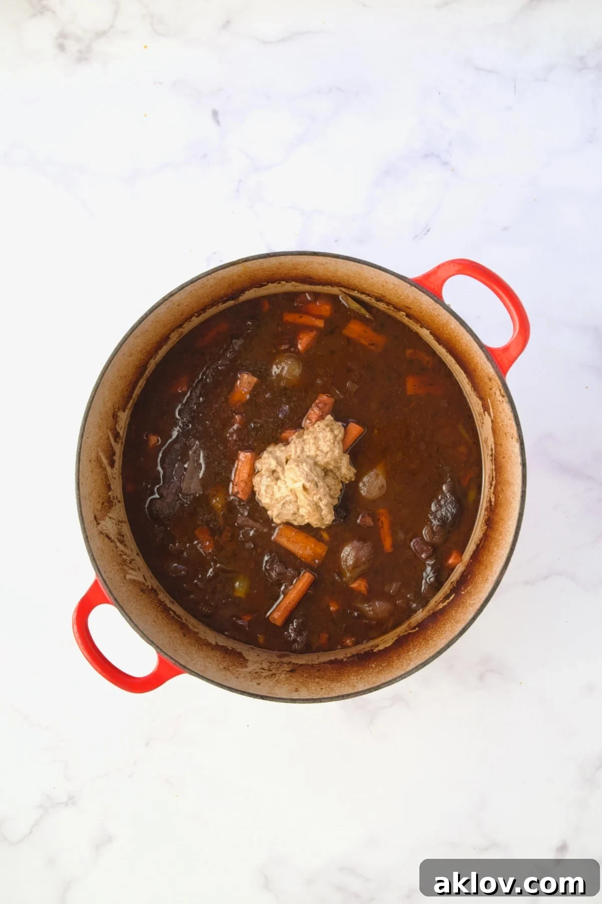 The thickening mixture carefully added to the bubbling stew in a red Dutch oven, ensuring a smooth sauce.