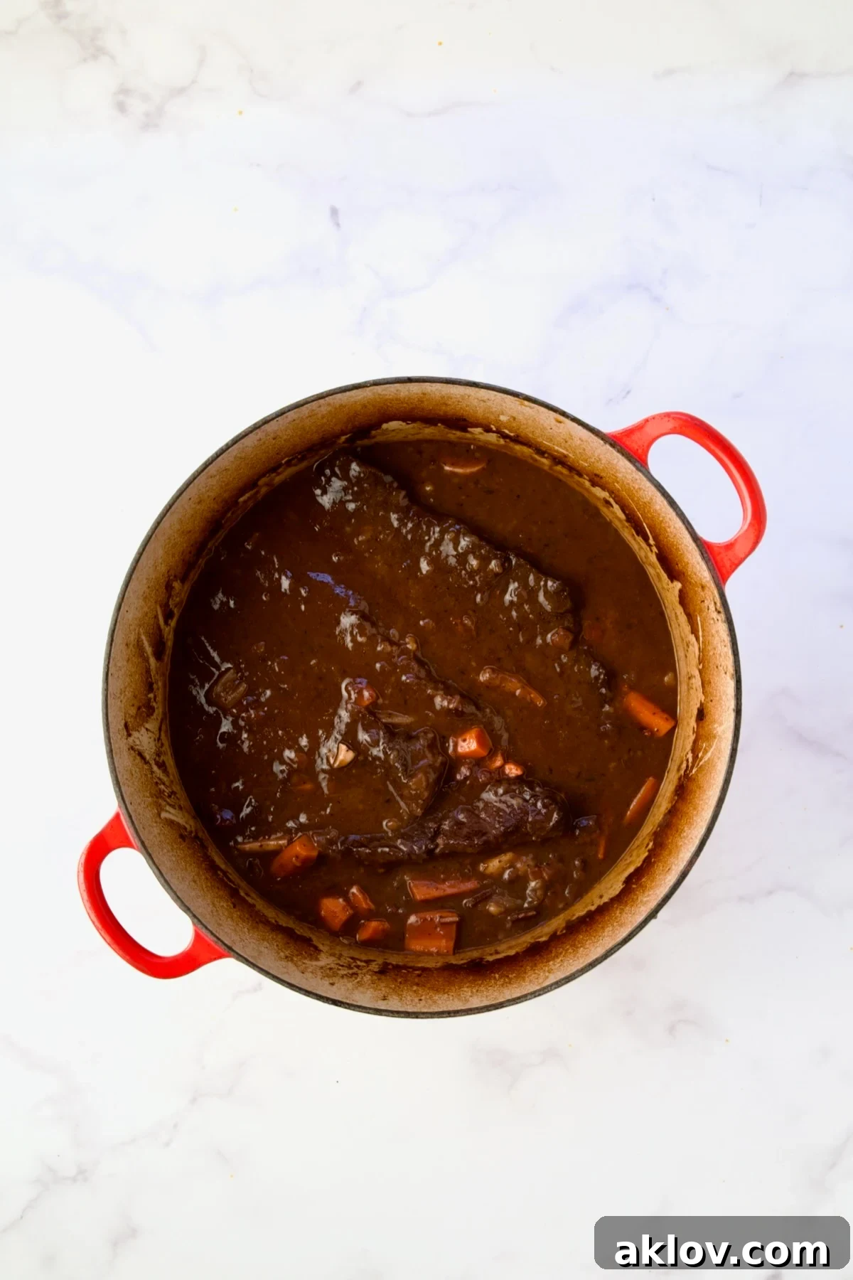 The rich, thickened Short Ribs Bourguignon stew simmering to perfection in a red Dutch oven.