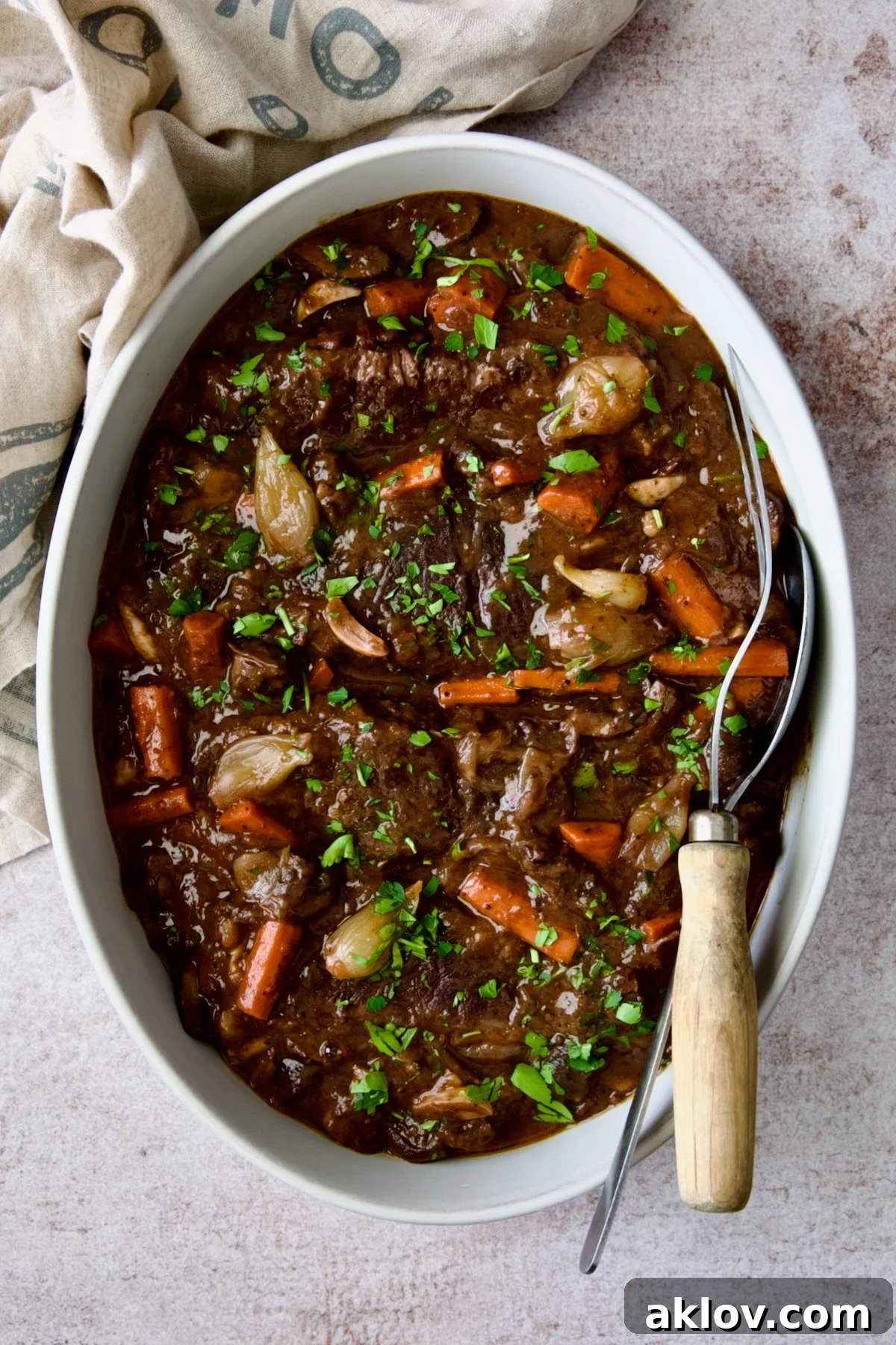 Serving dish filled with Boneless Beef Short Ribs Bourguignon and serving utensils, highlighting its rich texture.