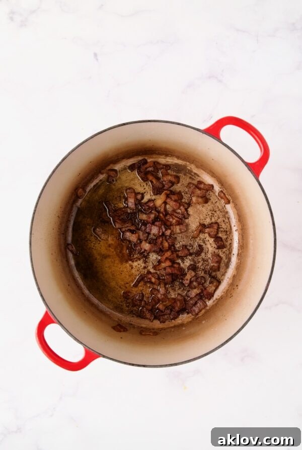 Perfectly browned bacon sizzling in a vibrant red Dutch oven, a foundational step for rich flavor.