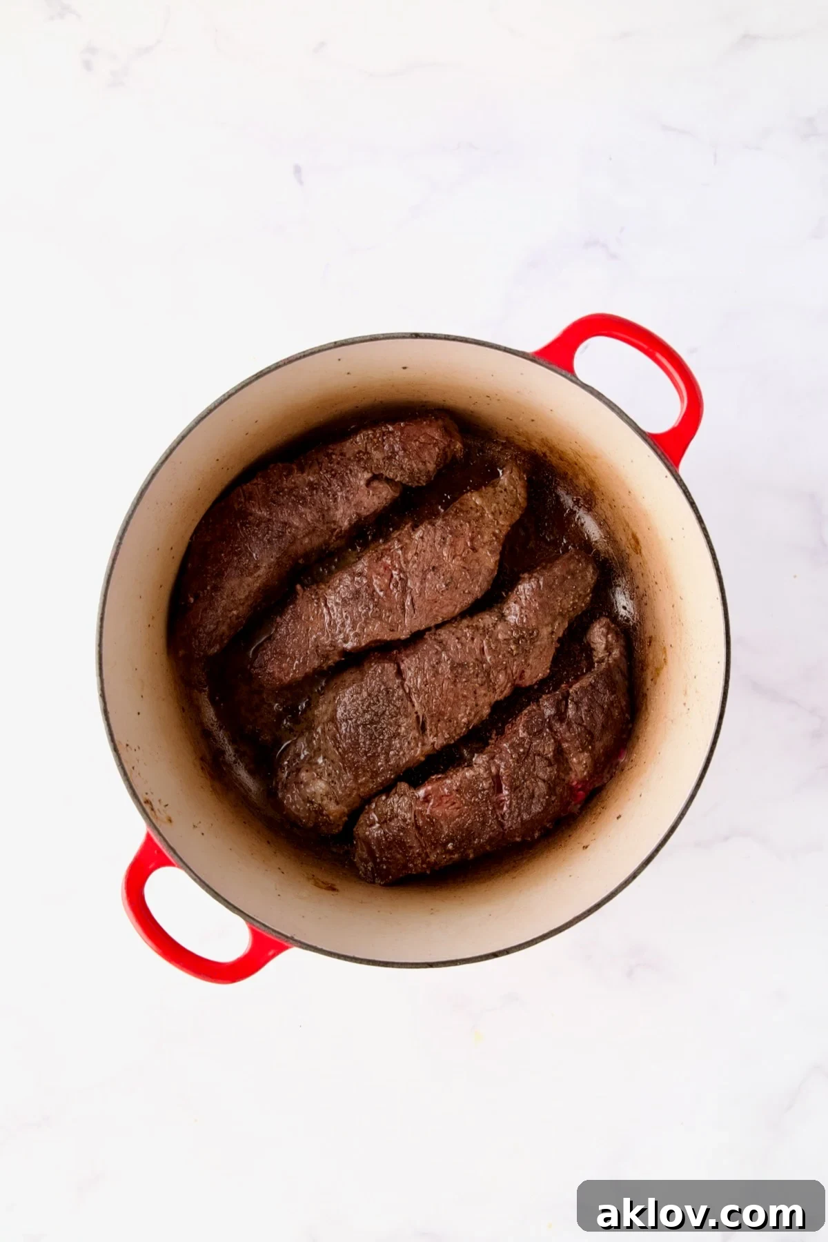 Four succulent boneless beef short ribs beautifully browned in a red Dutch oven, ready for the next stage.