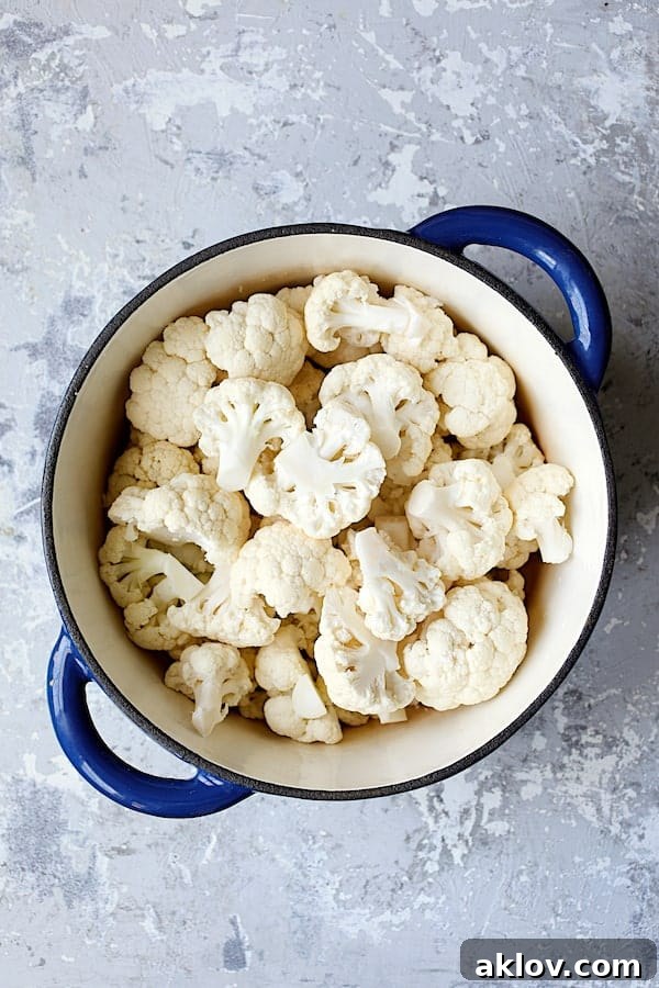 Uncooked cauliflower florets, chopped onion, garlic, and white beans resting in a vibrant blue Dutch oven, ready for simmering.