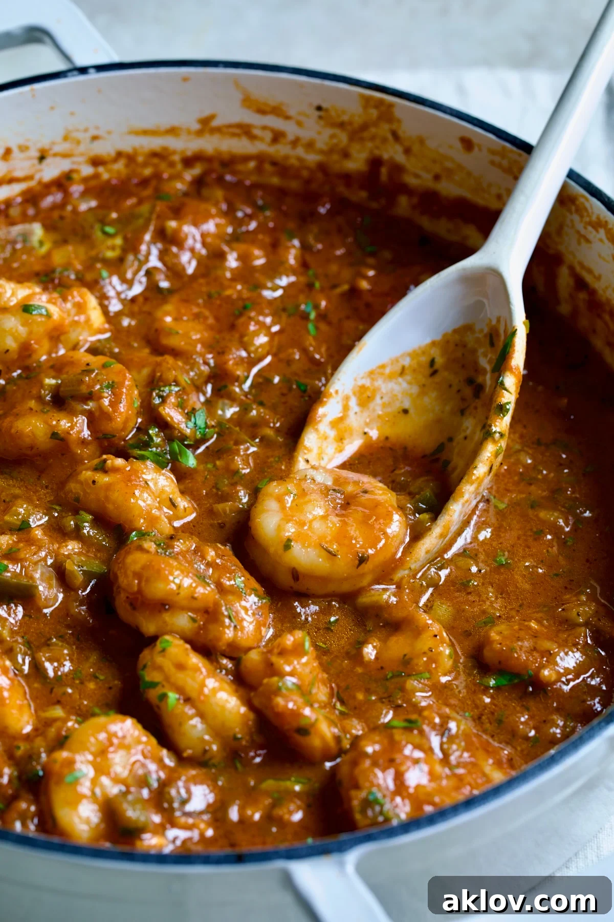 Finished Best Shrimp Creole in white enamel cast iron skillet with serving spoon scooping up one of the shrimp.