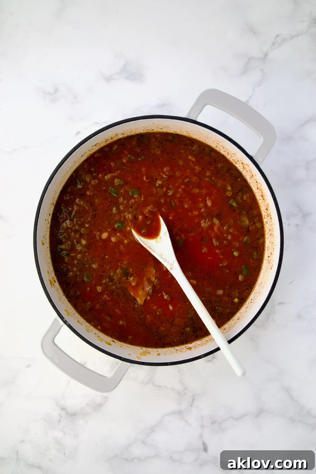 Tomato sauce and water added to vegetables and spices in white enamel cast iron skillet.