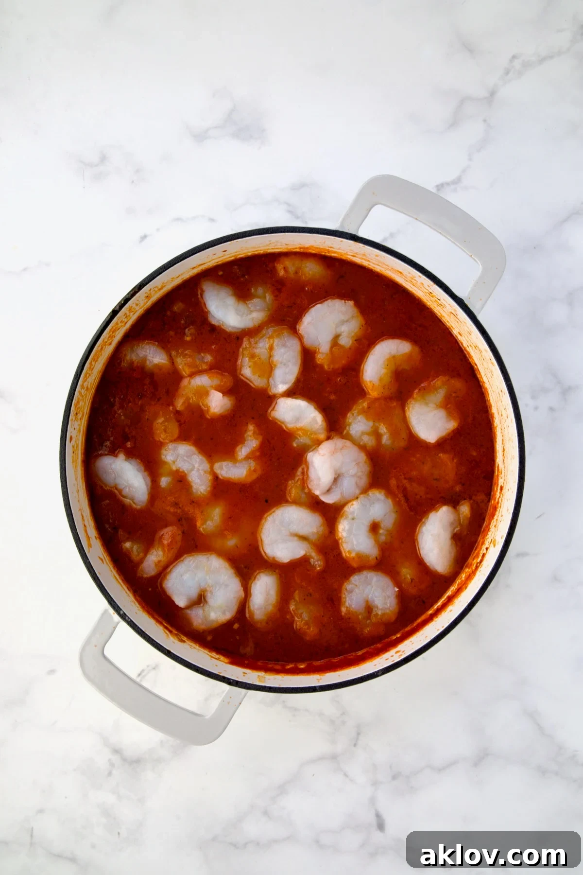 Uncooked shrimp added to tomato sauce in white enamel cast iron skillet.