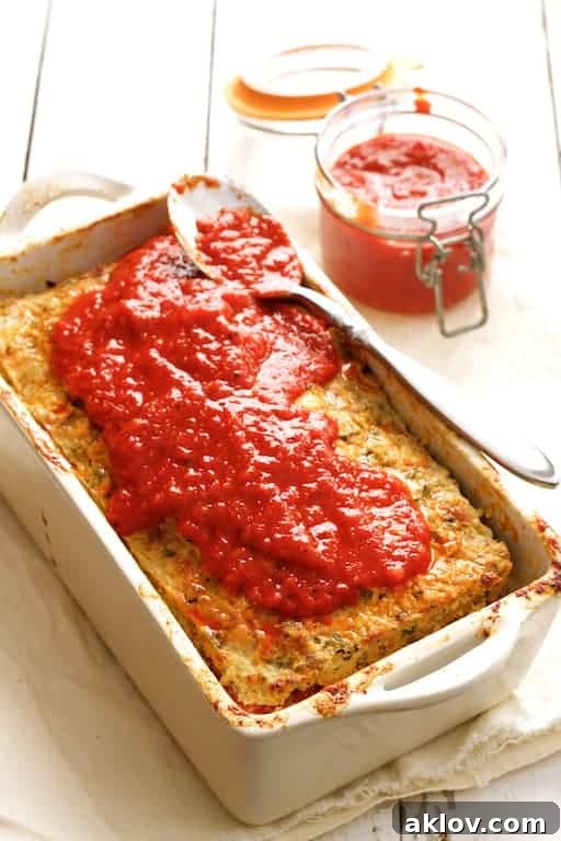 Photo of Layered Turkey Meatloaf with Roasted Red Pepper Sauce on white background with sauce partially spread over the top, showcasing its vibrant layers.