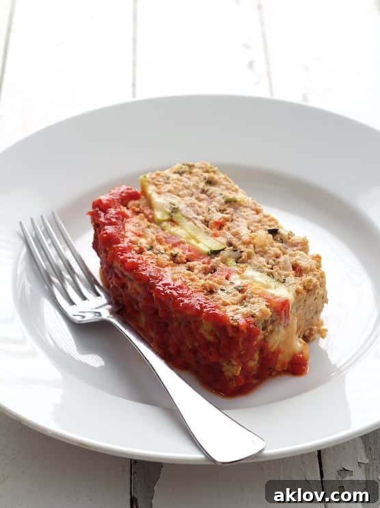 Photo of one slice of Layered Turkey Meatloaf with Roasted Red Pepper Sauce on white plate with fork, showing its tender texture.