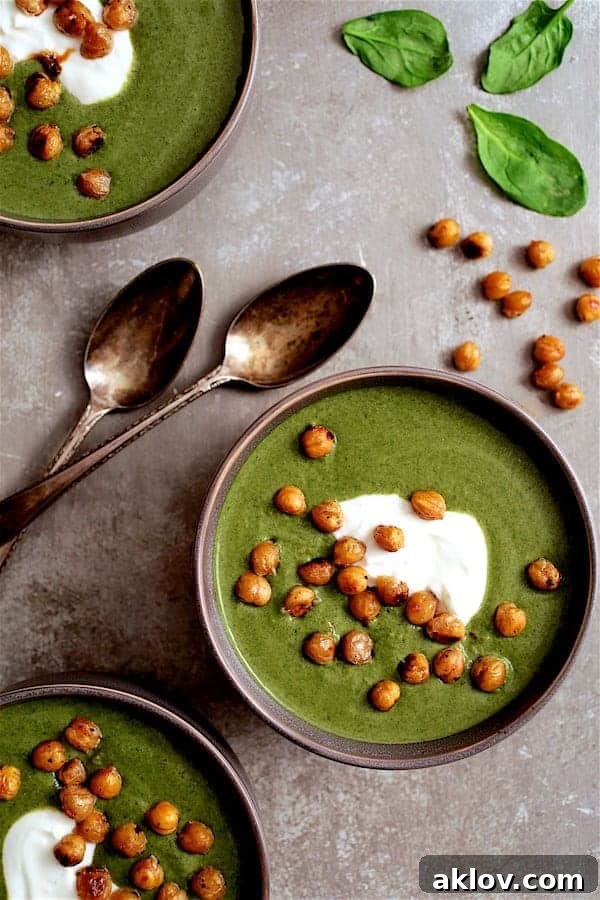 Photo of Spinach and Goat Cheese Bisque with Crispy Lemon Chickpeas on gray background, garnished with fresh herbs and a swirl of cream.