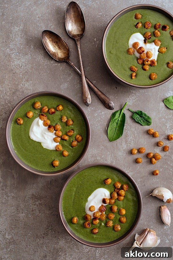 Photo of three individual servings of Spinach and Goat Cheese Bisque with Crispy Lemon Chickpeas garnished with Greek yogurt and fresh herbs on a rustic gray background.