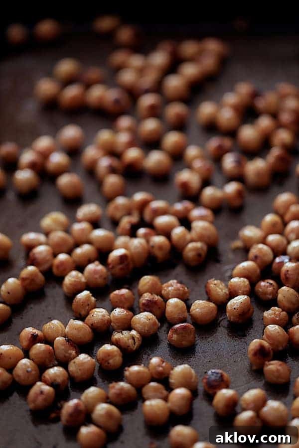 Photo of golden brown, crispy roasted chickpeas spread out on a baking sheet, glistening with lemon and olive oil.