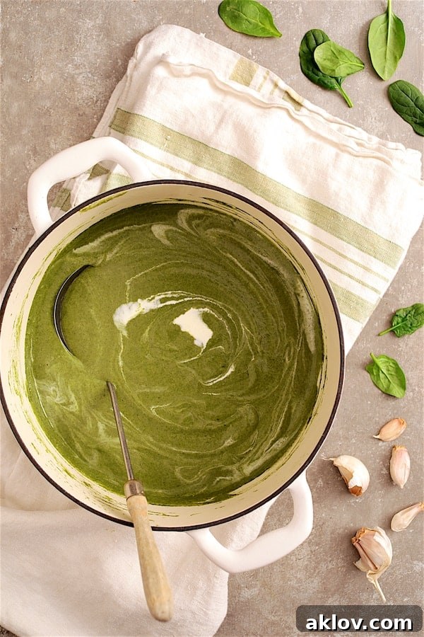 Photo of vibrant green Spinach and Goat Cheese Bisque simmering in a white Dutch oven, resting on a green striped towel.