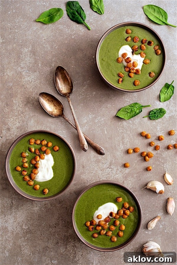 Photo of three bowls of creamy Spinach and Goat Cheese Bisque, beautifully garnished with a swirl of Greek yogurt and golden crispy lemon chickpeas.