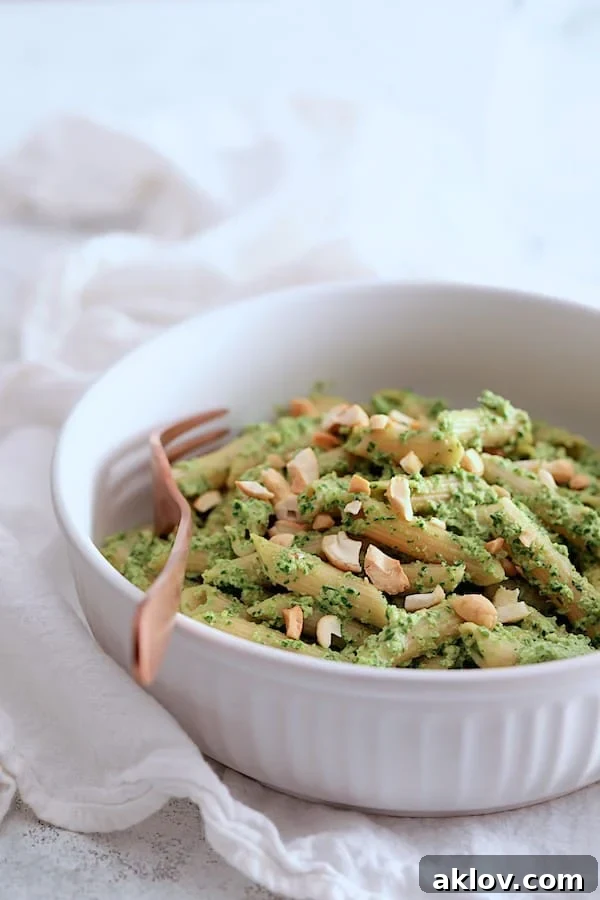 A captivating close-up of Penne with Creamy Cashew and Spinach Pesto Sauce, artfully presented in a white bowl, showcasing the rich texture and vibrant green hue of the pesto-coated pasta.