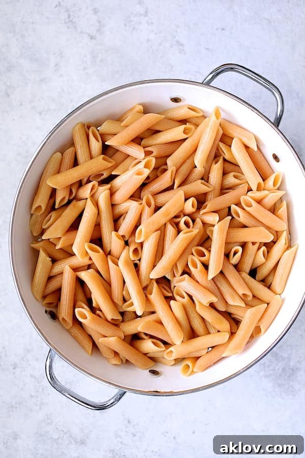 A clean, white colander cradling a generous portion of cooked Modern Table Penne Pasta, steam gently rising, signifying its perfect al dente readiness.