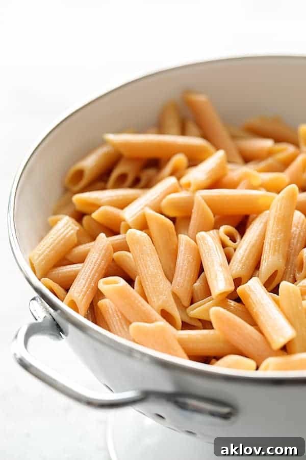 A detailed close-up shot of Modern Table Penne Pasta, perfectly cooked and nestled within a white colander, showcasing its texture and readiness for saucing.