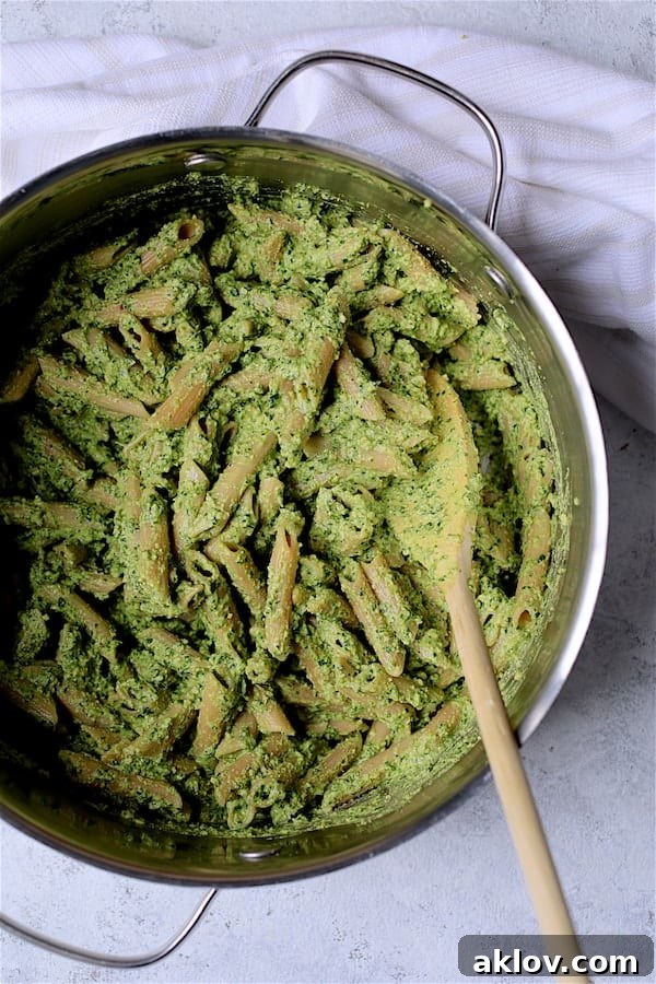 Photo of Penne Pasta with Creamy Cashew and Spinach Pesto Sauce being stirred in a cooking pot with a wooden spoon.