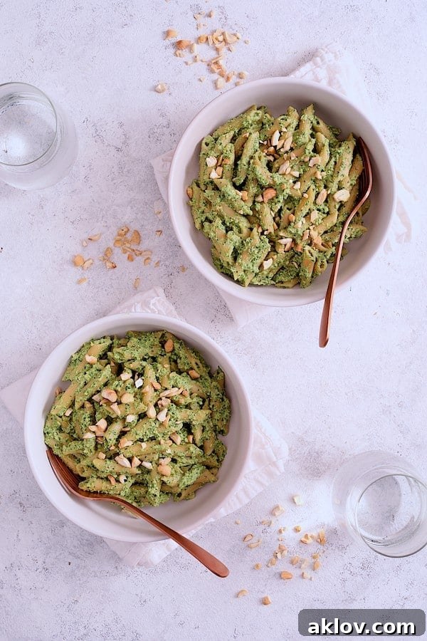 Two beautifully presented servings of Modern Table Penne Pasta with Creamy Cashew and Spinach Pesto Sauce, garnished with chopped cashews, invitingly placed on a clean white background.
