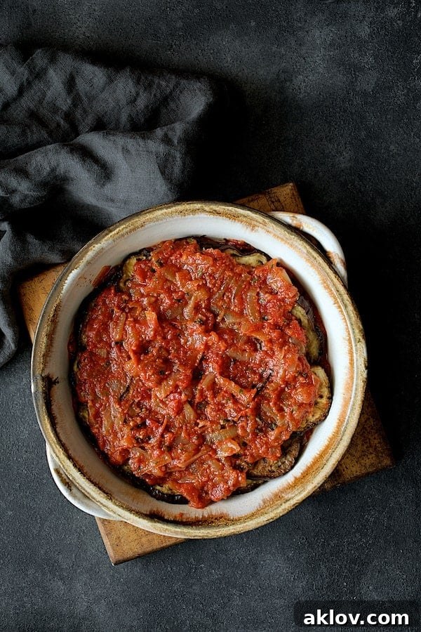 Photo of final later of tomato sauce placed over the top in baking dish. The casserole is topped with the last layer of vibrant tomato and onion sauce, ready for its final bake to perfection.