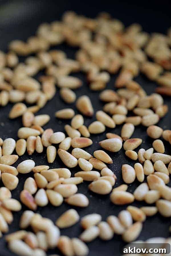 Photo of toasted pine nuts. A handful of golden-brown pine nuts are perfectly toasted, ready to add a crunchy, nutty finish to the dish.