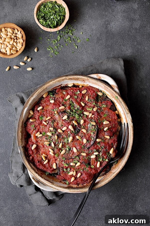 Photo of baked Turkish Eggplant Casserole - Imam Bayildi garnished with pine nuts and chopped parsley. The beautifully baked Turkish Eggplant Casserole (Imam Bayildi) is artfully garnished with toasted pine nuts and fresh chopped parsley, presenting a vibrant and inviting meal.