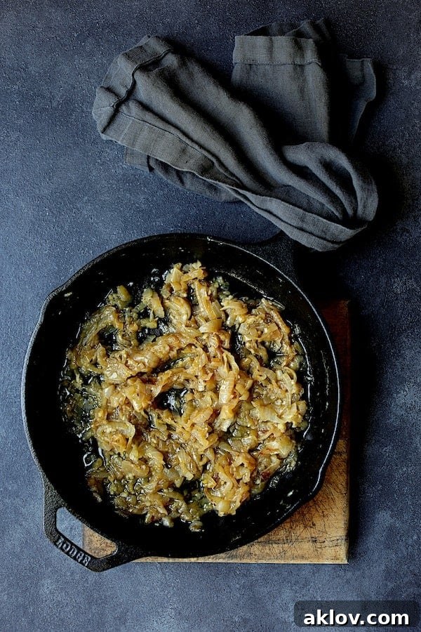 Photo of cooked onions in cast iron skillet. Sautéed onions, soft and translucent with hints of golden brown, gently simmer in a rustic cast-iron skillet, forming the flavorful base of the sauce.