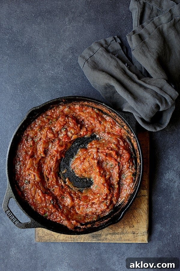 Photo of tomato sauce in cast iron skillet. A rich, vibrant tomato sauce, infused with spices and aromatics, bubbles gently in a cast-iron skillet, ready to be layered with tender eggplant.