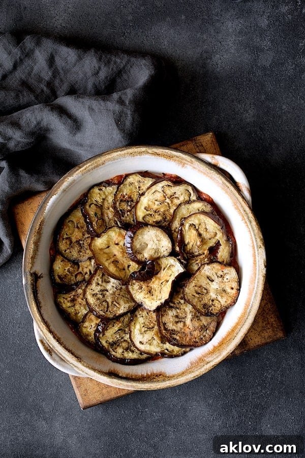 Photo of first layer of eggplant placed over tomato sauce in clay baking dish. Tender, baked eggplant slices are carefully arranged over the tomato sauce, creating the first aromatic layer in the clay baking dish.