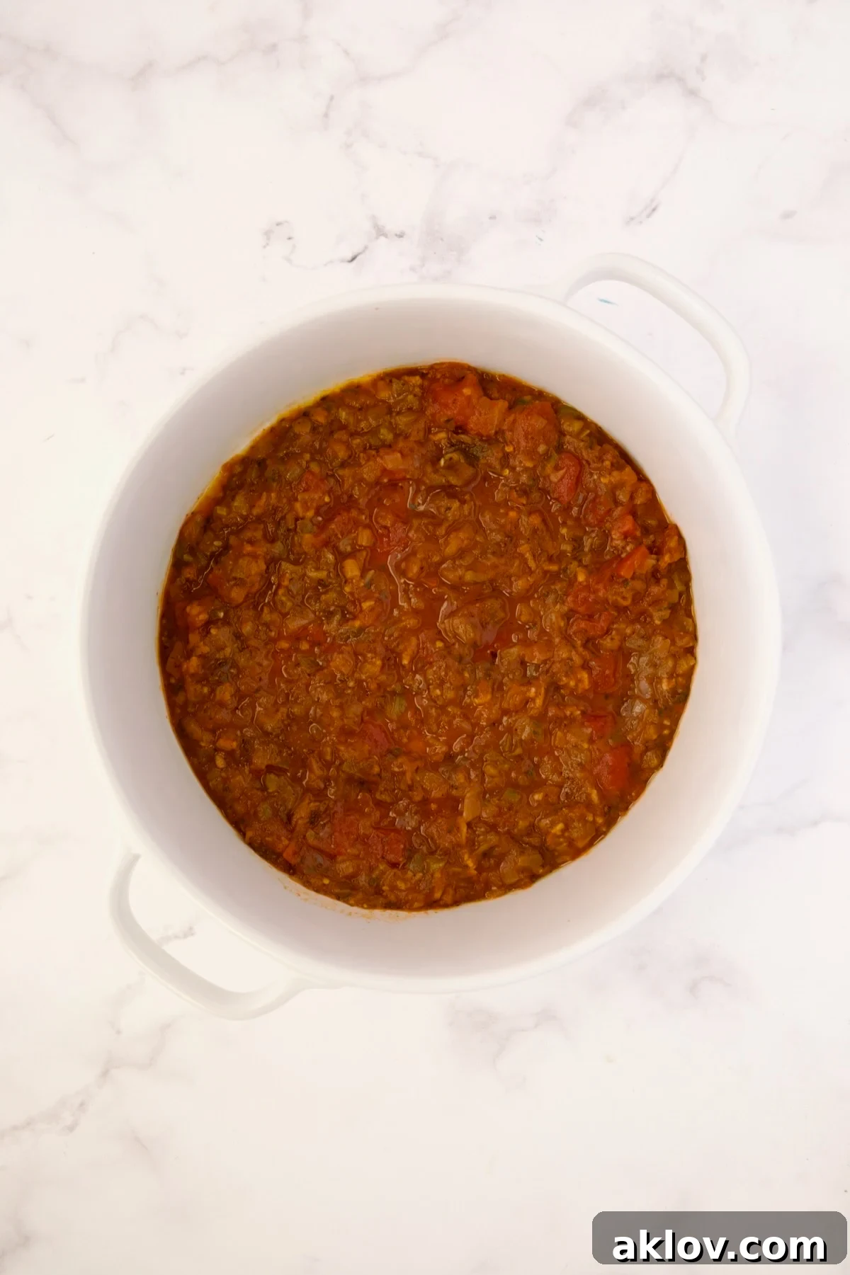 Tomato sauce spread on the bottom of a deep white round baking dish.