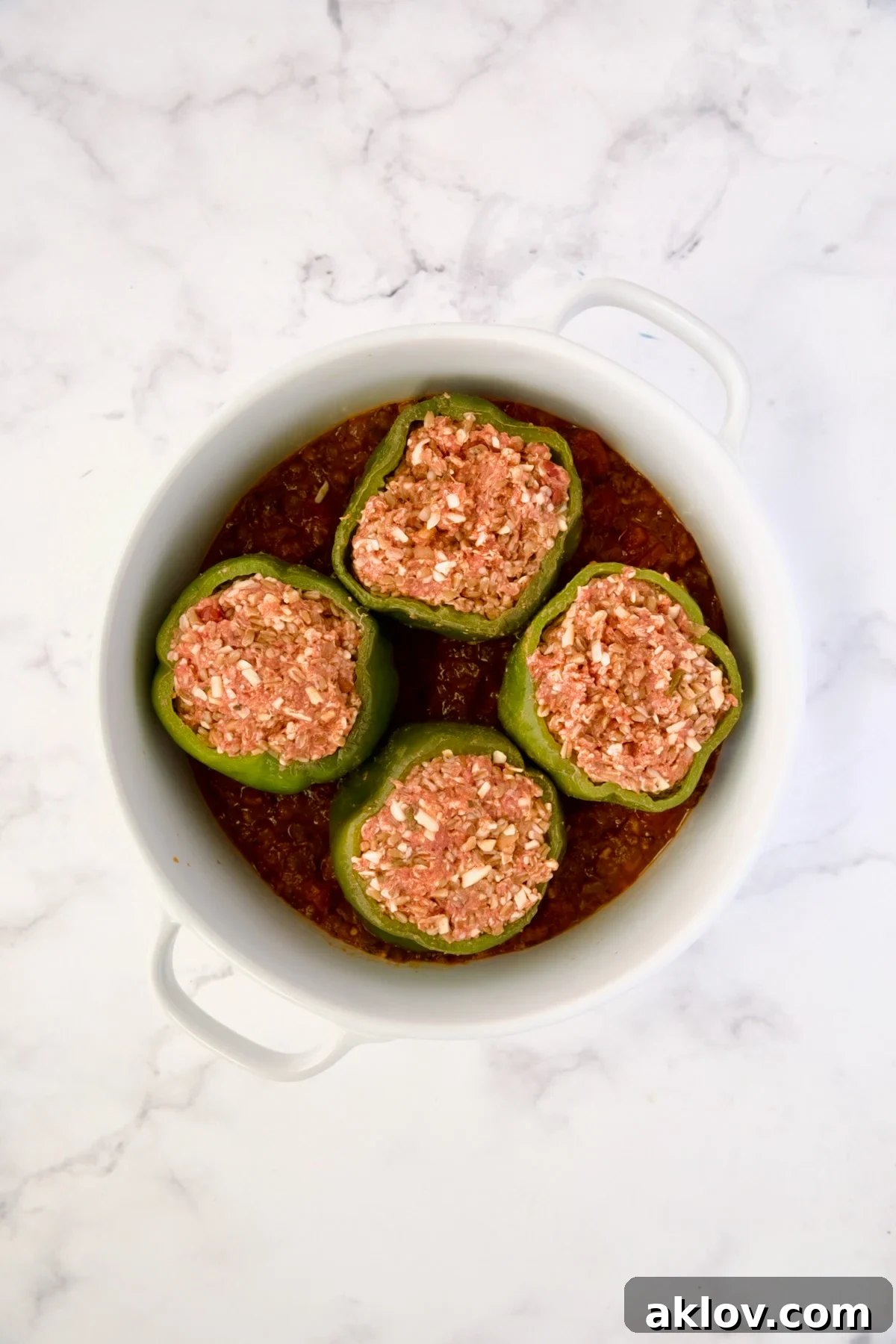 Filled bell peppers placed on the sauce in a baking dish, before more sauce is added.