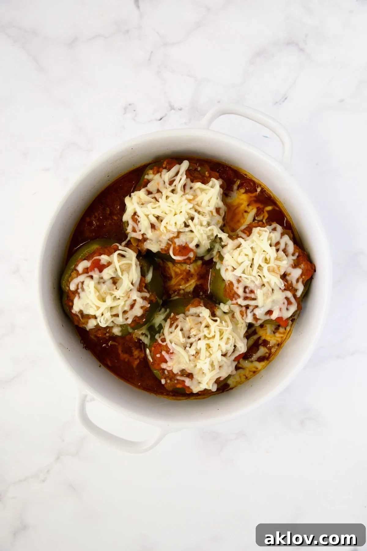 Baked bell peppers in a deep white round baking dish with melted cheese on top.